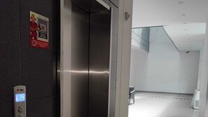 Ein moderner Aufzug mit digitaler Anzeige, ein sauberer Korridor mit Fliesenböden und ein Schild an der Wand.