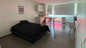 Ein modernes Schlafzimmer mit einem Bett, einem Schreibtisch und einem Stuhl. Ein kleiner Hund sitzt auf dem Bett.
