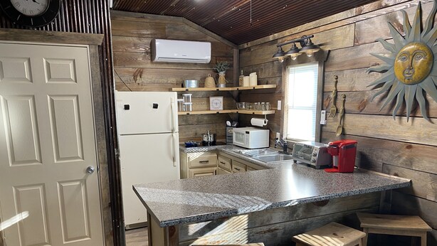 Una cucina con un piano di lavoro in granito, sgabelli di legno, frigorifero, microonde, tostapane e una parete in legno decorata con un motivo solare.