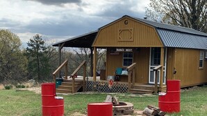 A wooden cabin with a porch, a sign reading "NANA'S NEST," and a fire pit area. - Quaint Country Cabin - Experience the Ozarks (CALICO ROCK)