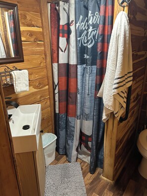 A bathroom with wooden walls, a sink, a toilet, a shower curtain with a pattern, and a towel hanging on the wall.