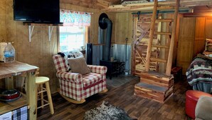 A cozy cabin interior with a wooden ceiling, a rocking chair, a television, a fireplace, and a staircase. - Quaint Country Cabin - Experience the Ozarks (CALICO ROCK)