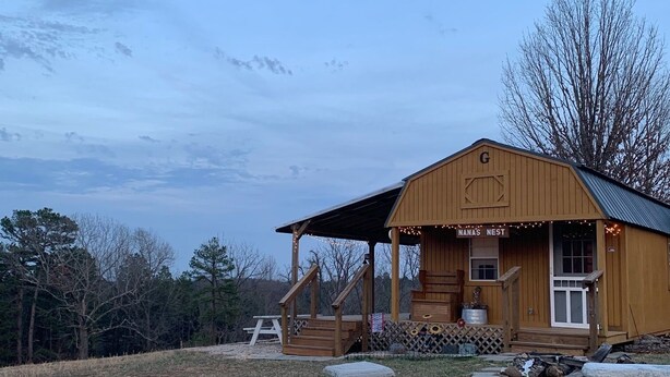 A wooden cabin with a porch, a sign reading "Manas Nest," and a picnic table in a grassy field. - Quaint Country Cabin - Experience the Ozarks (CALICO ROCK)