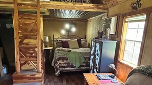 A rustic cabin interior with a wooden staircase, a bed with patterned bedding, a sofa, and a small table. - Quaint Country Cabin - Experience the Ozarks (CALICO ROCK)