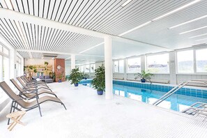 Une piscine intérieure moderne, dotée de chaises longues et de plantes en pot.