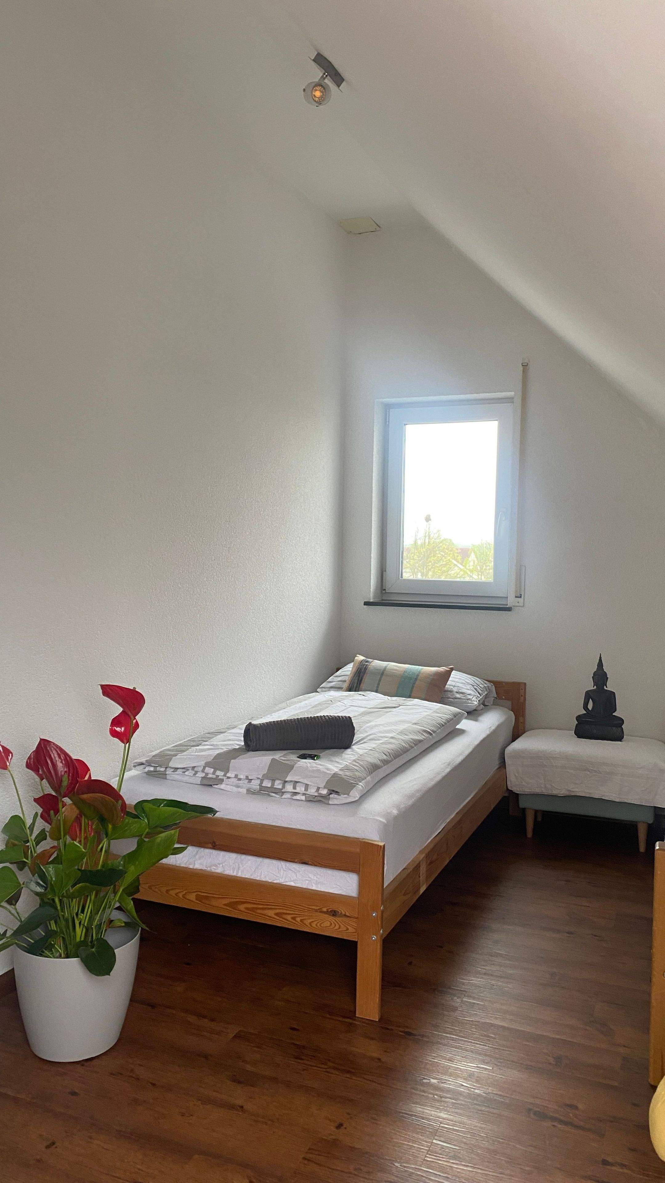 Une chambre à coucher avec un lit en bois, une fenêtre, un petit banc et une plante en pot.