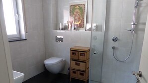 Uma casa de banho com sanita, chuveiro e um pequeno armário de madeira.