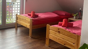 Quarto com duas camas de madeira, um vaso de planta e uma varanda com vista para edifícios.