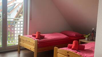 A room with two wooden beds, a potted plant, and a balcony with a view of buildings.