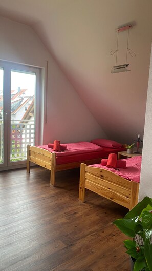 Una habitación con dos camas de madera, una planta en maceta y un balcón con vista a edificios.