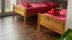 A room with two wooden beds, a potted plant, and a balcony with a view of buildings.