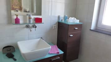 A bathroom with a white sink, a mirror, a glass shelf with toiletries, and a dark wooden cabinet.
