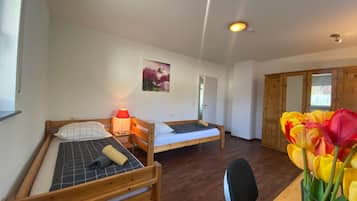 A room with two wooden beds, a small table, a chair, a wall-mounted lamp, and a door leading to another room.