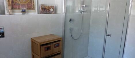 A bathroom with a glass shower enclosure, a toilet, and a wooden storage unit.