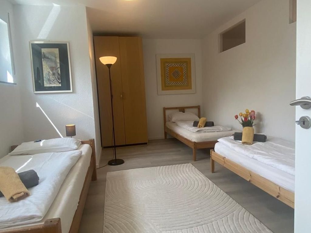 Una habitación con dos camas individuales, una lámpara de pie grande, un armario de madera y una obra de arte enmarcada en la pared.