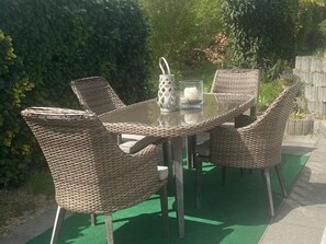 Une table ronde avec des chaises en osier, un porte-bougie en verre et un verre contenant une bougie.