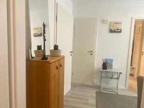 Käytävässä on puinen kaappi, valkoinen ovi ja pieni pöytä, jonka päällä on taulu.