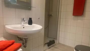 Een badkamer met een wit wastafel, een spiegel, een douche en een toilet.