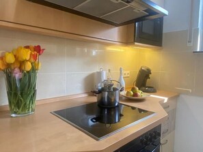 Une cuisine moderne équipée d’une cuisinière intégrée, d’un four à micro-ondes placé au-dessus et d’un vase en verre contenant des tulipes, posé sur le plan de travail.