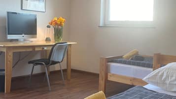Une chambre à coucher avec un lit en bois, un bureau avec un ordinateur, une chaise, une fenêtre et un téléviseur fixé au mur.