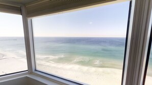 A view from a window overlooking a beach with a pier in the distance.