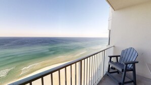 A balcony with a view of the ocean, a chair, and a railing.