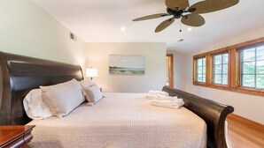 A hotel room with a large bed, a ceiling fan, a painting on the wall, and a window with a view. - Spacious Getaway with Sauna, Close to Newport & Beaches (Middletown)