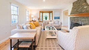 A spacious living room with a stone fireplace, two sofas, a coffee table, and a patterned rug. - Spacious Getaway with Sauna, Close to Newport & Beaches (Middletown)