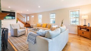 A spacious living room with a sofa, armchairs, and a coffee table. There is a staircase leading to another level, and a wooden cabinet with a lamp. - Spacious Getaway with Sauna, Close to Newport & Beaches (Middletown)