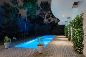 A swimming pool with a wooden deck, surrounded by trees and plants.