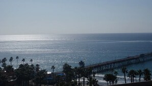 Vista costera con un muelle que se adentra en el océano, palmeras y un cielo despejado.