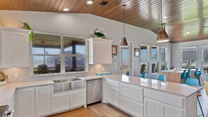 A modern kitchen with white cabinetry, a central island, and pendant lighting. - The Neon Moon - 3rd Row Coastal beauty, close to the beach w/ Gulf Views! (Port Bolivar)
