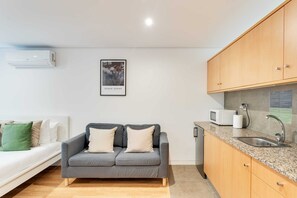A modern kitchen with a grey sofa, wooden cabinets, and a microwave.