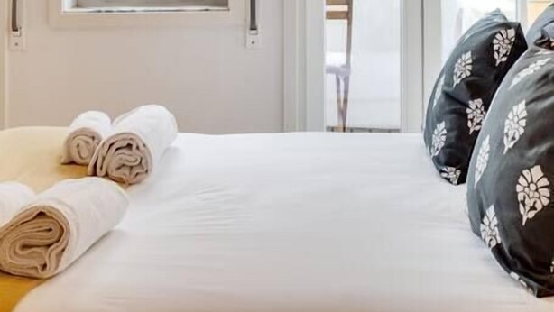 Hotellihuone, jossa on sänky, rullalle taitetut pyyhkeet ja näkymä ulkopuolella olevalle parvekkeelle.
