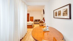 A hotel room with a wooden dining table, a bed, a sofa, and a wall-mounted picture.