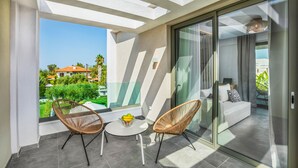 Een balkon met twee rieten stoelen, een kleine tafel met een schaal fruit, en uitzicht op een woonwijk.
