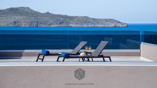 A rooftop terrace with two sun loungers, a table with drinks, and a view of the sea and a distant hill. - Brand New Luxury villa★Sauna & Jacuzzi★Walk to Everything★Private Heated Pool (Galatas)