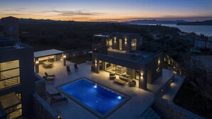 A modern two-story house with a swimming pool, outdoor seating, and a view of the sea at dusk. - Brand New Luxury villa★Sauna & Jacuzzi★Walk to Everything★Private Heated Pool (Galatas)