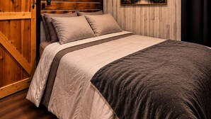 Une chambre à coucher avec un lit en bois, un tableau représentant une forêt et une porte en bois.