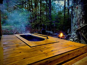 A wooden deck with a hot tub in a forested area.