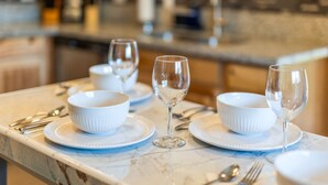 A marble countertop with white bowls and wine glasses set for a meal.