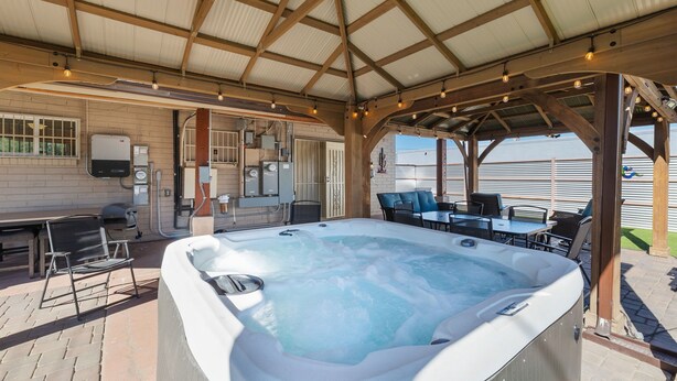 A covered outdoor area with a hot tub, seating, and a patio table.