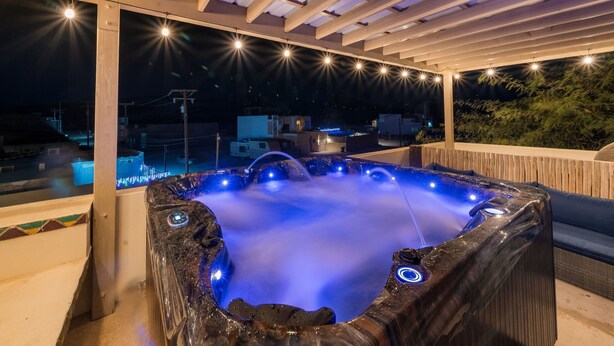 Ein Whirlpool unter einer Pergola mit Lichterketten, umgeben von einer Holzterrasse mit Blick auf eine Wohngegend.