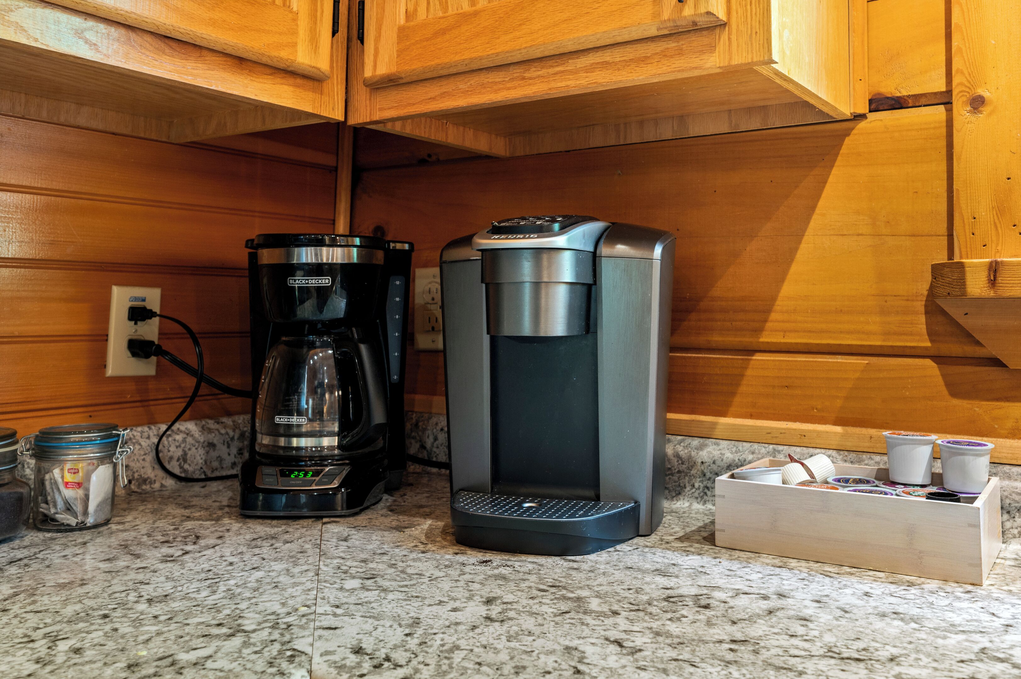 A kitchen with a coffee maker and a water dispenser, a wooden cabinet, and a marble countertop.
