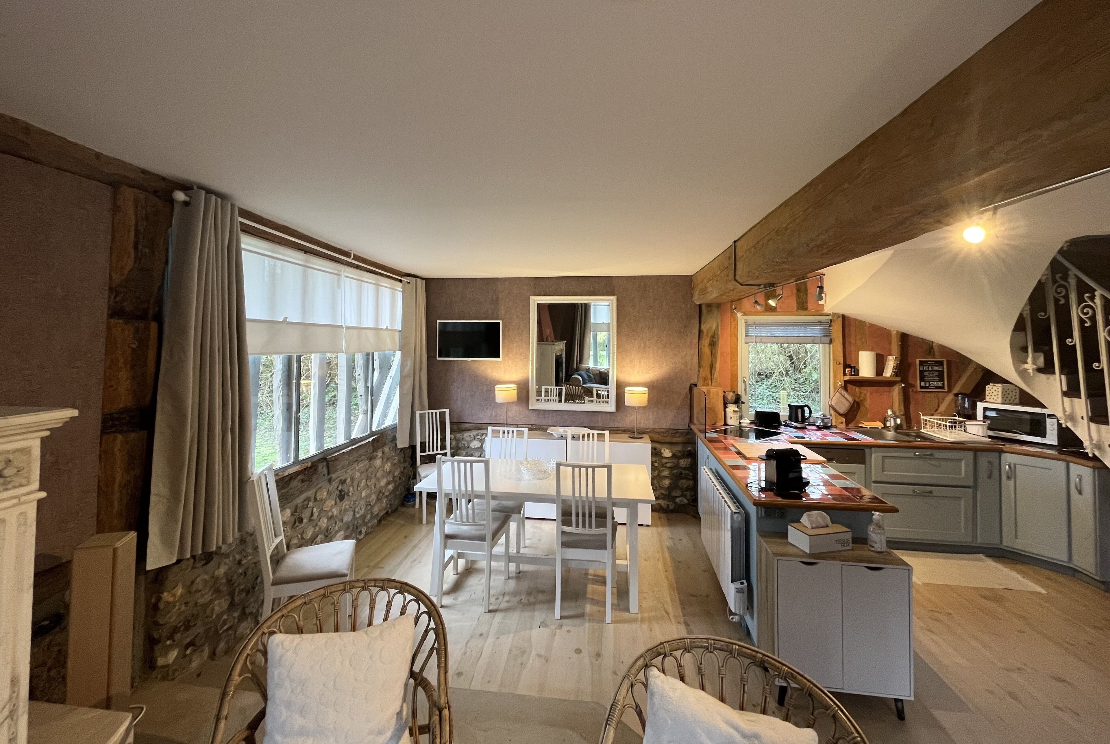 Un coin repas chaleureux avec un mur en pierre, une grande fenêtre avec des rideaux et une table à manger blanche, assortie de chaises.