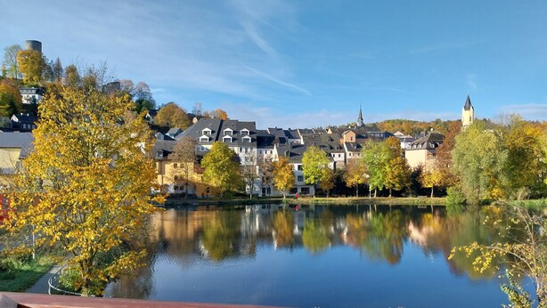Vista de un lago con un pueblo, edificios y una torre de iglesia.