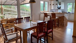 Un comedor con mesa y sillas de madera, un jarrón con flores y vistas a un jardín a través de amplios ventanales.