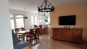 Amplia sala de estar con sofá, mesa de comedor, sillas y televisor montado en la pared.