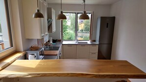 Una cocina con encimera de madera, armarios blancos, un refrigerador y una ventana con vistas a edificios y árboles.