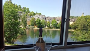 Una botella de vino y dos copas sobre una mesa junto a una ventana con vistas a un río y edificios.